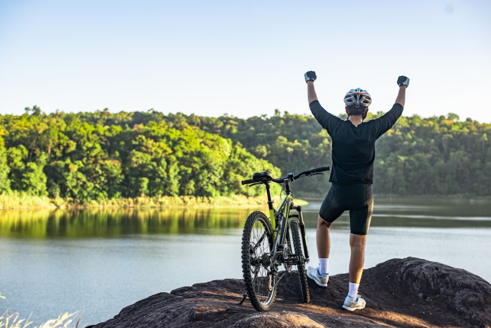 man with his hands up standing on a rock near a lake, coast with trees in front of him